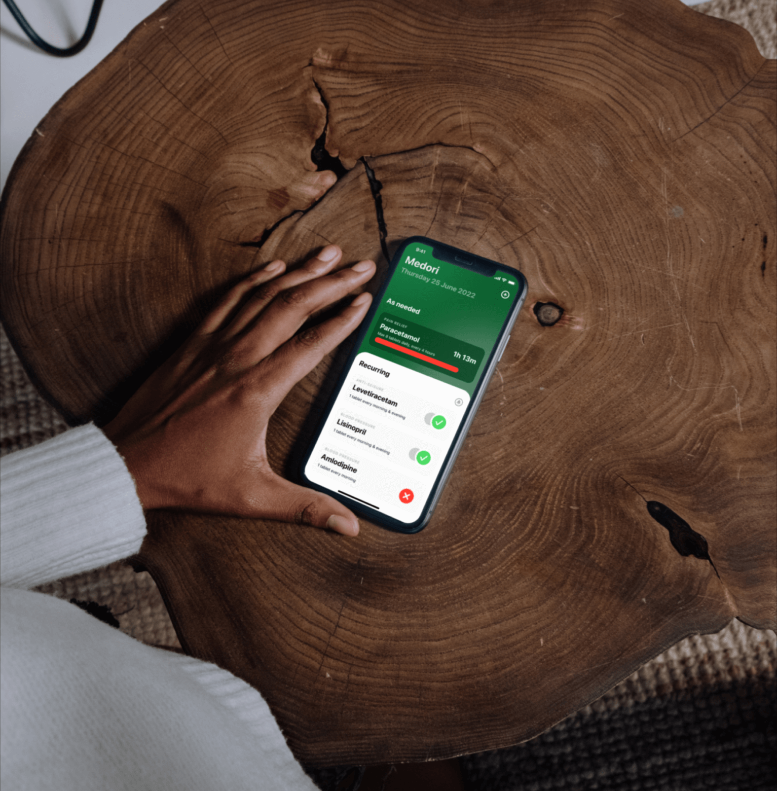 A person's hands holding a phone displaying the Medori app which lists medications and which have been taken